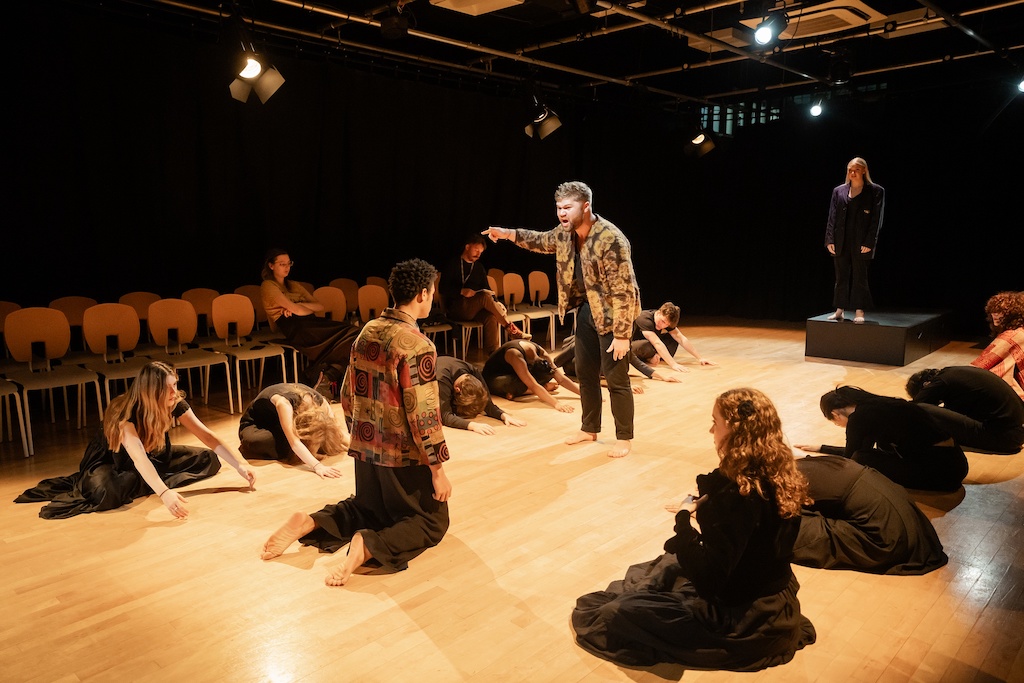 An actor kneels in front of another actor who is angrily pointing as other actors bow or kneel on stage during the final presentation of The Winter's Tale.